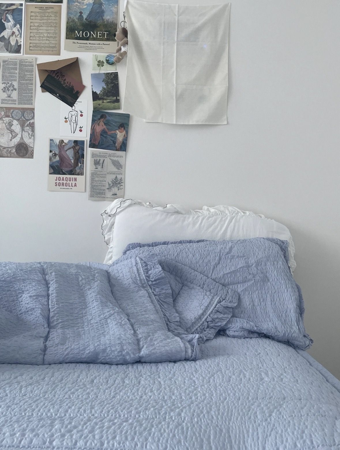 아이보리 바탕에 푸른 침구가 깔린 침대. 벽면에는 모네의 포스터와 엽서, 강아지 키링이 보인다. / 이미지 출처: 필자 촬영