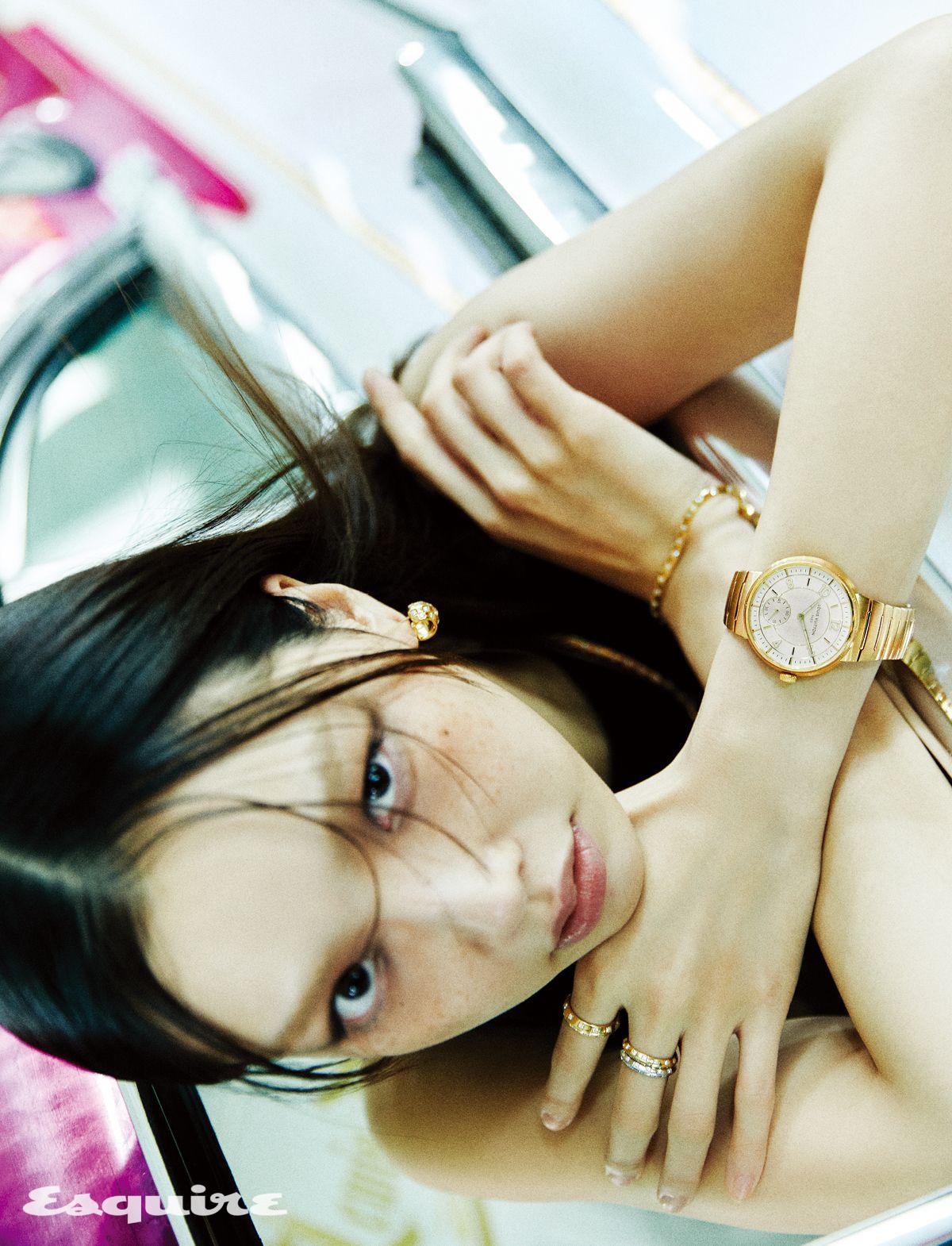 40mm 옐로 골드 케이스와 일체형 브레이슬릿의 땅부르 워치, 옐로 골드 르 다미에 드 루이 비통 이어링, 옐로 골드 르 다미에 드 루이 비통 미디엄 네크리스, 옐로 골드 르 다미에 드 루이 비통 미디엄 브레이슬릿, 검지에 착용한 옐로 골드 르 다미에 드 루이 비통 미디엄 링, 중지에 레이어링한 화이트 골드와 옐로 골드 르 다미에 드 루이 비통 스몰 링, 러플 디테일 블랙 미니드레스 모두 루이 비통.