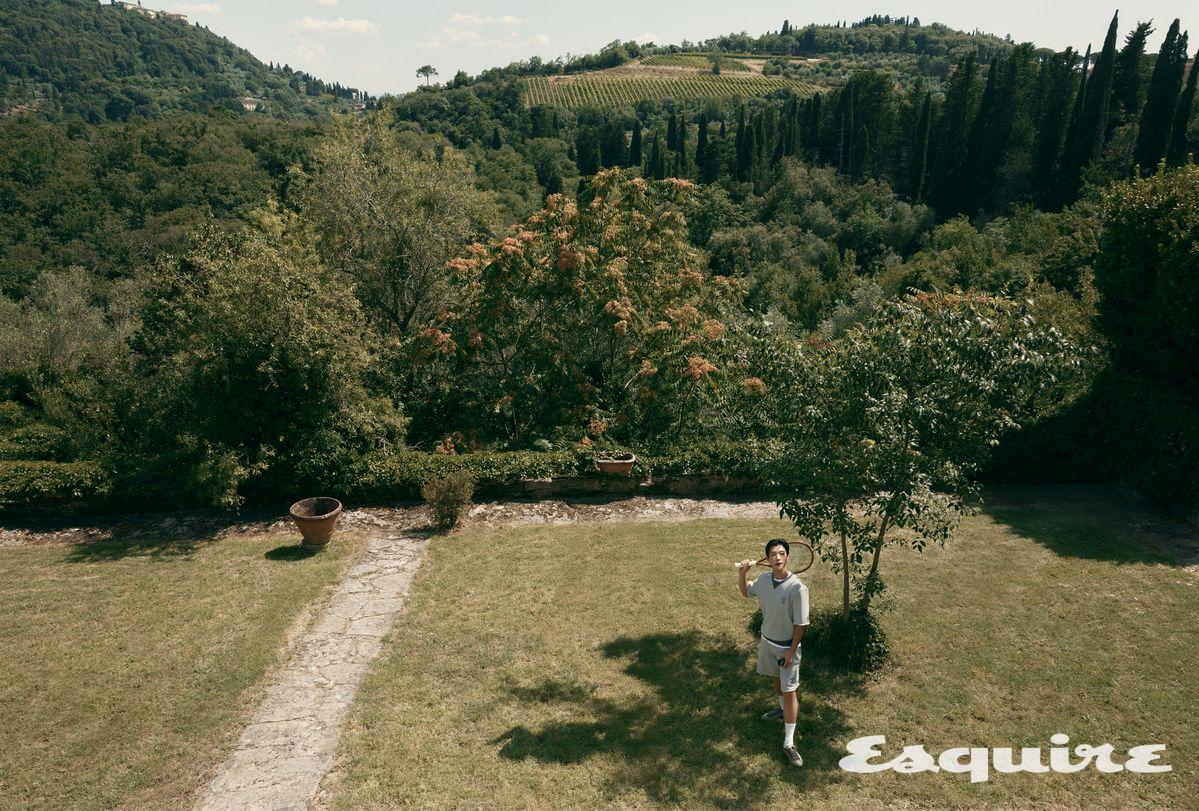 자수 디테일의 반소매 티셔츠, 화이트 티셔츠, 버뮤다 쇼츠, 화이트 삭스, 레더 스니커즈, 테니스 라켓 모두 브루넬로 쿠치넬리.