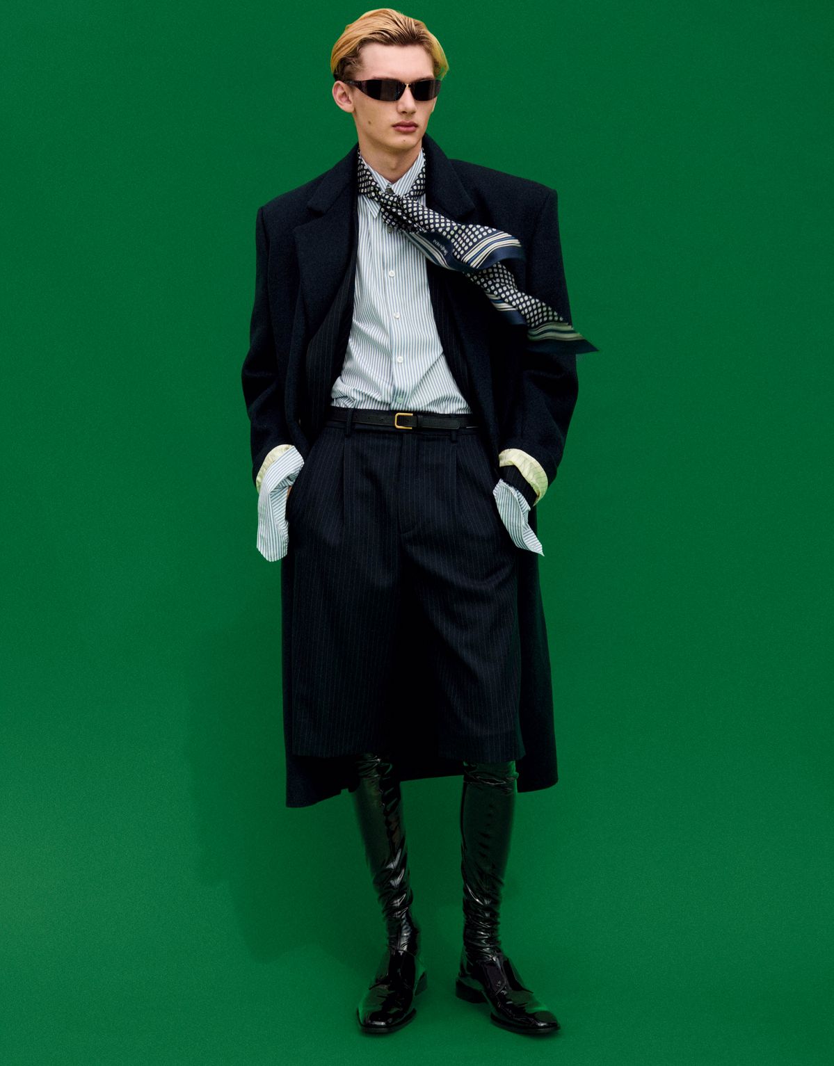 블랙 울 코트, 스트라이프 울 재킷, 화이트 스트라이프 셔츠, 스트라이프 울 쇼츠, 페이턴트 오버 더 니 부츠, 오벌 선글라스, 실크 스카프, 레더 벨트 모두 생 로랑 by 안토니 바카렐로.